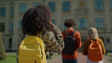 Arkaya bakan çok ırklı öğrenciler üniversitede yürürken Afrikalı kız kameraya bakıp gülümsüyor. Çeşitlilik gösteriyor. Üç kız arkadaş.