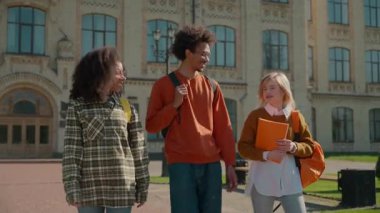 Üç çok ırklı öğrenci birlikte yürüyorlar. Üniversite kampüsünün dışında konuşuyorlar. Afrikalı Amerikalı erkek, beyaz, kadın, kız arkadaşlar lisede iletişim kuruyorlar.