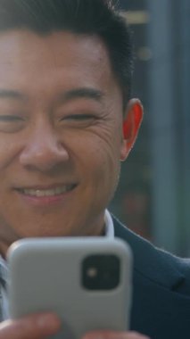 Mutlu gülümseyen Asyalı orta yaşlı iş adamı... Koreli iş adamının cep telefonu uygulaması ile sohbet ediyor... elinde akıllı telefon aygıtı, siber uzay... Japon erkek, uzak teknolojide çalışıyor.