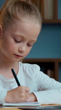 Beyaz tenli küçük öğrenci kız öğrenci kız öğrenci notlar yazıyor. Uzaktan eğitim alıyor. Akşamları dizüstü bilgisayar çalışmalarına bakarak ev ödevleri yazıyor.