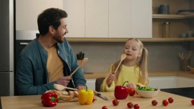 Kafkasyalı mutlu aile mutfakta şarkı söylüyor baba kızıyla kahvaltı hazırlıyor baba çocuk babasıyla eğleniyor çocuk kaşık içinde şarkı söylüyor mikrofon gibi birlikte gülüyor