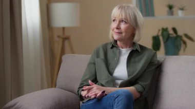 Düşünceli, yaşlı, düşünceli, beyaz bir kadın. Evine bakıyor. Kanepede dinleniyor. Yetişkin bir kadın.