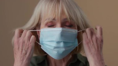 Yakın plan beyaz kadın. Kapalı alanda, bej renkli stüdyoda tıbbi yüz maskesi portresi çıkarıyor. Salgın salgını durdurma salgını sona eriyor.