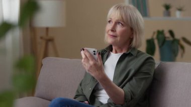 Yaşlı beyaz kadın telefonuna bakıyor. 60 'lı yaşlarda rahat bir kadın. Mobil uygulama internet alışverişi yapıyor.