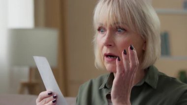 Şaşırmış Kafkasyalı yaşlı kadın elinde yüksek fiyatlı makbuz kağıdıyla ev şoku faturası bütçe mağazası giderlerinde son sınıf emekli kadın büyükannesinin şokunu hissediyor.