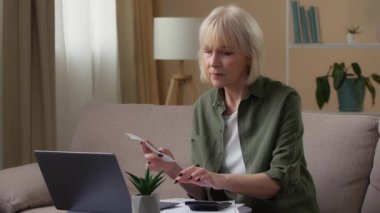 Aile bütçesini yöneten yaşlı beyaz bir kadın. Fatura çekiyle para sayıyor. Laptop hesap makinesiyle finansal krediyi kontrol ediyor.