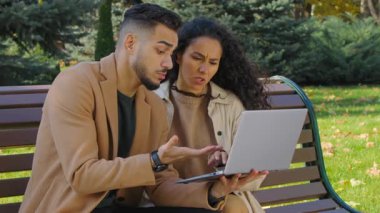 Laptop 'u olan endişeli İspanyol çift, sonbahar parkında, bankta problemleri tartışırken kafası karıştı. Bankta oturan Arap bir adam ve bilgisayar başında konuşan bir adam, sorun çözme sorunu internet üzerinden alışveriş yapmakta zorlanıyor.