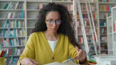 Sıkıntılı İspanyol Arabistanlı kadın öğrenci kütüphanede patinaj okuyor. Üniversite öğrencisi. Sınav başağrısı, baş ağrısı kitabı okuyor.