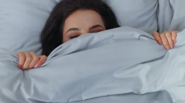 Kapalı kapılar ardında beyaz kadın battaniyenin altına saklanıp gülüyor kameraya bakıp gülüyor dişlek gülüyor dişlek, flört eden kız uyanıyor ve sabah yatağında yatıyor.