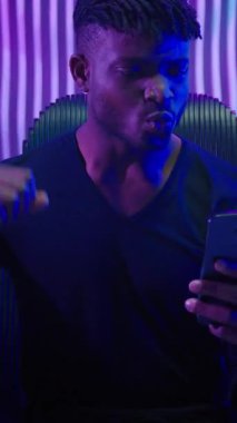 Siyah neon fütüristik uzay adamının cep telefonuyla kazandığı Afrikalı Amerikalı adam akıllı telefonuyla online yenilik siber uzay fütürizm teknolojisinin tadını çıkarıyor.