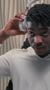 Futuristic African American ethnic man in headphones listening music move with hands funny dance freedom joy in white futurism studio male guy enjoying weekend pleasure radio listen song singing happy