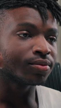 Headshot African American ethnic cyber man put on wireless headphones smiling looking at camera resting on chair in futuristic modern studio futurism space male guy smile having fun listening music