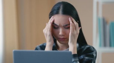 Evde dizüstü bilgisayar başında çalışan, başı ağrıyan, stresli, yorgun, Asyalı bir kadın. Baş ağrısı çeken Japon öğrenci, iş kadını, yönetici, evde gerginlik, migren rahatsızlığı yaşıyor.