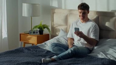 Mutlu beyaz erkek, evinde oturmuş gülümsüyor. Akıllı telefon kullanan genç adam cep telefonuyla mesajlaşıyor internette sohbet ediyor. Mesaj yolluyor.