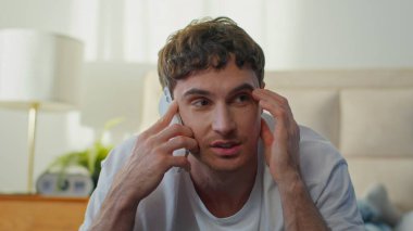 Neşeli, gülümseyen, beyaz bir genç adam yatak odasında akıllı telefonuyla konuşuyor. Mutlu Avrupalı iş adamı gülen cep telefonuyla konuşuyor.
