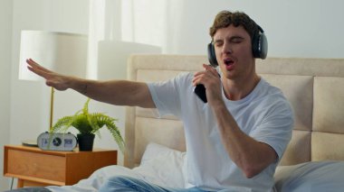 Aktif Kafkasyalı adam yatak odasında uzanıyor kulaklık takıyor müzik dinliyor erkek sesli eğleniyor alet kulaklıkları kullanıyor evde kablosuz çalma listesi teknolojisi gevşemesi kullanıyor