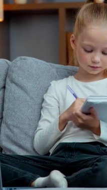 Kafkasyalı çocuk kız çocuk kanepede e-öğrenim kursu notlar yazarak öğretmenlere cevap yazarak çalışma ve sanal online oturma odasında ders sırasında dizüstü bilgisayara bakarak ev ödevi yapıyor.