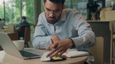 Etnik Hintli iş adamı, para şirketinin bütçesini hesaplayan veriler yazıyor. Not yazıyor. Kafe 'de çalışan masa başı erkek yöneticisinin bilgisayarlı bankacılık hizmeti veren Arap işadamının makbuzunu kontrol ediyor.