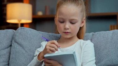 Kafkas odaklı küçük kız çocuğu ev ödevi yapıyor ilköğretim öğrenimi hazırlık sınavları okuyor not defterine sevimli öğrenci kız öğrenci eğitim kitabı yazıyor.