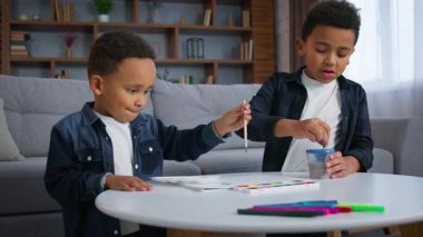 İki Afrikalı Amerikalı çocuk boya boyuyor eve odaklanmış çocuklar okul çocukları etnik erkek kardeşler kardeş renkli resimler çiziyorlar mutlu aile sanatı el yapımı el yapımı sanat aktiviteleri