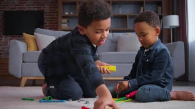İki etnik çocuk, Afrikalı Amerikalı çocuklar evlerinde oyuncaklarla, oğullarla, kardeşlerle, çocuklarla oynuyorlar. Çocuklar, evin içinde oyun oynayan aile kurmak için tamirat aletlerini kullanarak yenileme oyunu oynuyorlar.