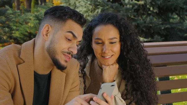 Sonbahar parkında birlikte cep telefonu kullanan çok ırklı Latin kökenli neşeli çift ekranda yemek siparişi vermeyi seçiyor.