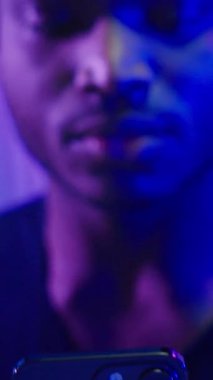 Afrikalı Amerikalı adam cep telefonuyla kazanmak için bağırmaktan mutlu. Karanlık neon fütüristik uzay tasasız kazananı erkek akıllı telefonla zaferi kutluyor. Fütürizm teknolojisi elde ediyor.