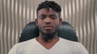 Kendine güvenen ciddi Afrikalı Amerikalı adam kameraya bakıyor. Gelecekteki etnik erkek oyuncu yüzüne bakıyor. Modern fütürizm beyaz odada sakin yüz ifadesine bakıyor.