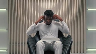 Concentrated African American man guy male put on headphones opening laptop typing hacking innovative cyberspace technology modern computer software in futuristic room game addicted online futurism