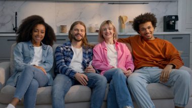 Çok ırklı bir arkadaş grubu evde kanepede oturup televizyon seyrediyor. Birlikte gülüyorlar. Kafkasyalı erkekler, Afrikalı Amerikalı kızlar, gülümseyen kızlar.