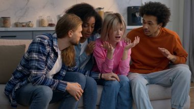 Multiethnic friends comforting upset crying Caucasian woman African American girl at home couch men women diverse buddies supporting helping calm soothe care stress friendly emotional support inside