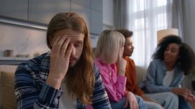Endişeli Kafkasyalı adam evde yalnız düşünüyor endişeli endişeli dışlanmış endişeli erkek arkadaş stresi çekiyor çoklu etnik kadınlar birlikte eğlenirken erkekler sosyal dışlanma izolasyonu yaşıyor