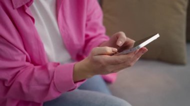 Tanımlanamayan beyaz bir kadın evinde oturuyor, cep telefonu yazıyor, sohbet ediyor, cep telefonu kullanıcısı, akıllı telefon uygulamasını tarıyor, sosyal medya internetinden alışveriş mesajları yazıyor.