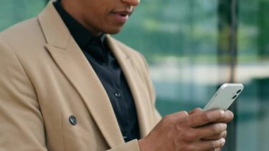 Afro-Amerikan iş adamının şehir dışında cep telefonu tutmasını kutlarken mutlu ol. Erkek girişimci işadamı iş adamı, akıllı telefona bakıyor. Zafer kazan.