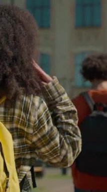 Arkaya bakan çok ırklı öğrenciler üniversitede yürürken Afrikalı kız kameraya bakıp gülümsüyor. Çeşitlilik gösteriyor. Üç kız arkadaş.