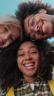 Alttaki görüntüde gülümseyen çok ırklı öğrenciler el sallıyor. Kamera önünde el sallıyorlar. Üç farklı etnik çeşitlilikteki arkadaş.