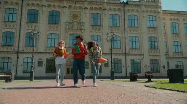 Three multiracial students walking university celebrating throwing books in air girls African American women Caucasian female boy man guy male leave college high school talking in city education break