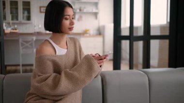 Kanepedeki beyaz İspanyol kadın akıllı telefon online alışveriş siparişi kadın ev sahibi kanepe rahatlatıcı kadın kullanıcı nüfuzlu cep telefonu internet uygulaması bağımlılık teslimatı satın alıyor