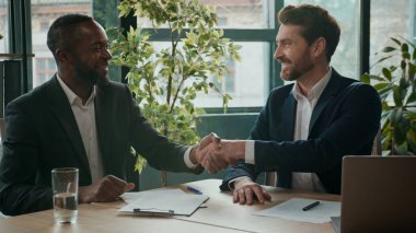Gülümseyen iki başarılı iş adamı sigorta şirketinin elini sıkıyor şirket anlaşması imzalıyor ortaklık ortaklığı işadamları Kafkasyalı Afrikalı Amerikalı işverenler ofiste