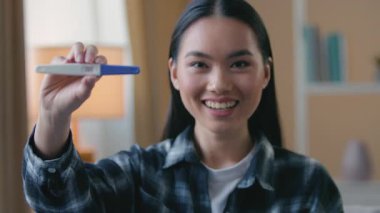 Mutlu hamile Japon kadın, elinde pozitif hamilelik testi, gülümseyen Asyalı anne kadın doğurganlık, neşe, neşe, tıbbi bakım, doğum kontrolü, aile planlaması.