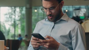 Arap iş adamı Hintli işadamı kafeteryada cep telefonu ekranına bakıp kötü haberler okumaktan endişeli, endişeli erkek uzman ziyaretçi akıllı telefon sosyal medya sorunundan rahatsız.