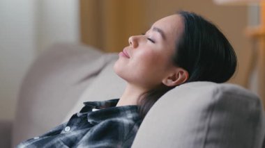 Yan görüş sakin Asyalı kadın gözlerini kanepeye kapatıp dinleniyor Japon kadın kanepede uzanmış uyukluyor zaman uyukluyor huzurlu yaşam tarzı dinlenme odası rahatlığı