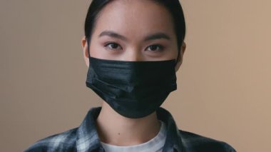 Siyah tıbbi maske takan Asyalı kadın portresi. Kapalı mekanda jest yaparken gülümseyen Çinli kadın. Yüz onayı tavsiyesi.