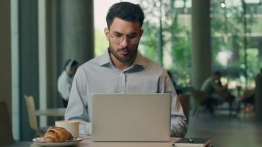 Bilgisayarlı konsantre Hintli işadamı kafeteryada kruvasanla çay içiyor bilgisayar işi yapan Arap işadamı ciddi profesyonel internet işçisi