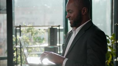 Gülümseyen etnik adam, Afro-Amerikalı iş adamı laptopuyla şirket ofisinde çalışan yetişkin erkek yönetici çevrimiçi dijital veri analizi inceleme bilgisayarında çalışıyor.