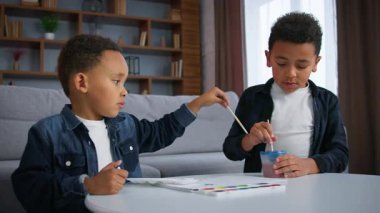 İki Afrikalı Amerikalı çocuk resim yaparken çocuklara ilham verdi. Etnik küçük kardeşler. Erkek kardeşler, düşünceli bir aileyi suluboya resimlerle birlikte resmettiler.