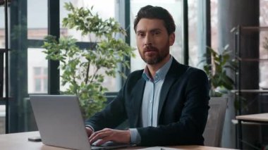 Beyaz iş adamı dizüstü bilgisayarını yazarken gülümsüyor. Kamera fotoğrafına bakıyor. Profesyonel erkek girişimci. İK yöneticisi.