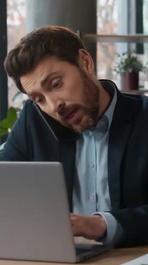 Kafkasyalı çoklu görev sahibi iş adamı bilgisayarlı bilgisayarda cep telefonuyla konuşuyor. Ofiste profesyonel iş adamı erkek menajer. Uzaktan kumandayı içeride kullanan müşteriye danışıyor.