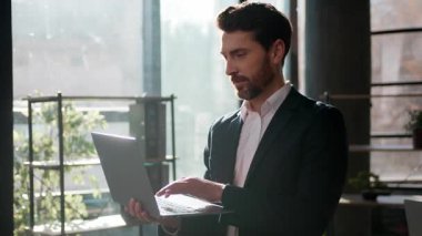 Ofiste sabahleyin dizüstü bilgisayarı daktilo eden, kendine güvenen beyaz iş adamı, güler yüzlü, profesyonel erkek lider yönetici, bilgisayar yöneticisi, kapalı mekanda çalışan iş adamı başarısı.