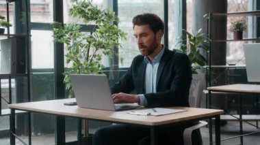 Düşünceli şaşkın Kafkasyalı ofis işadamı bilgi analizi yaparken bilgisayar uzmanı erkek girişimci yönetici kullanarak notlar yazıyor iş adamı adam.